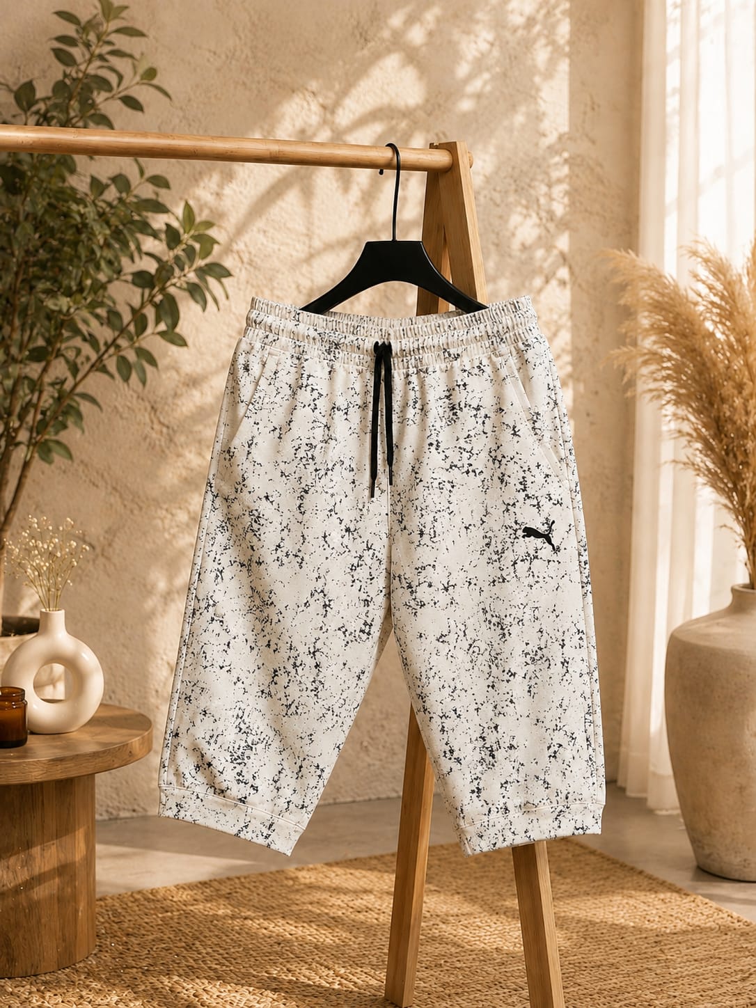 White and black printed men’s shorts with an elastic waistband, drawstring, and relaxed fit, hanging on a wooden clothing rack.
